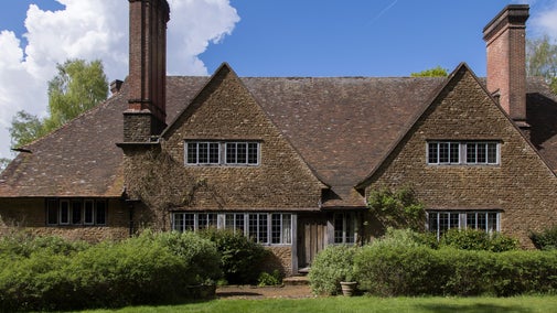Brick and stone south elevation to the house at Munstead Wood. The ground floor of the house is partially hidden by bushy shrubs.